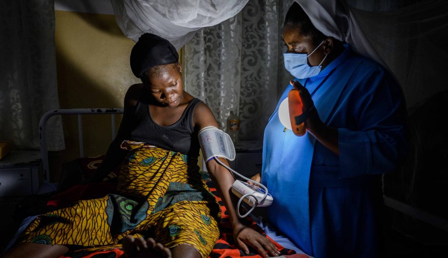 Siter Grace takes a pregnant lady's blood pressure using a solar light.