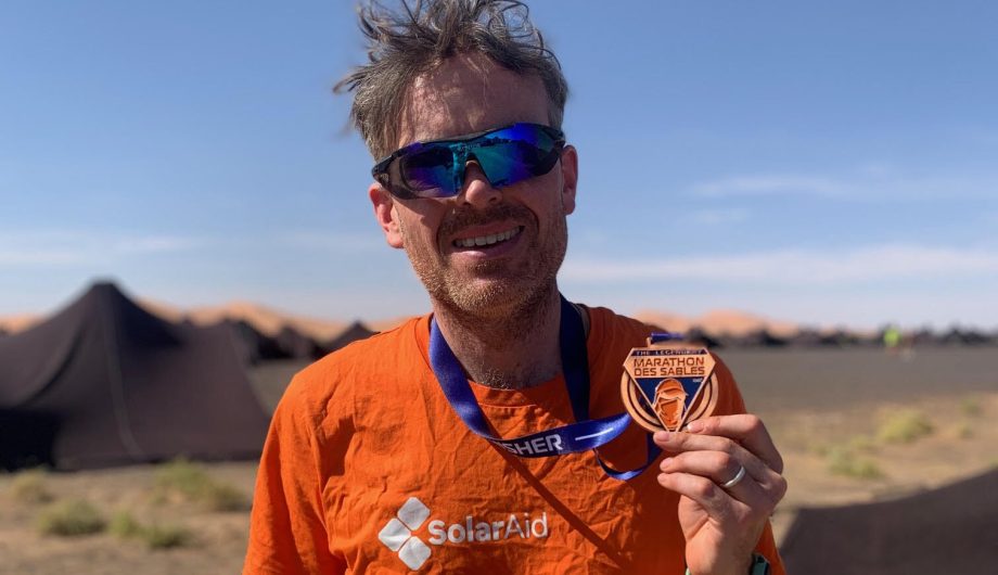 Man holds medal from Marathon des Sables in the desert.