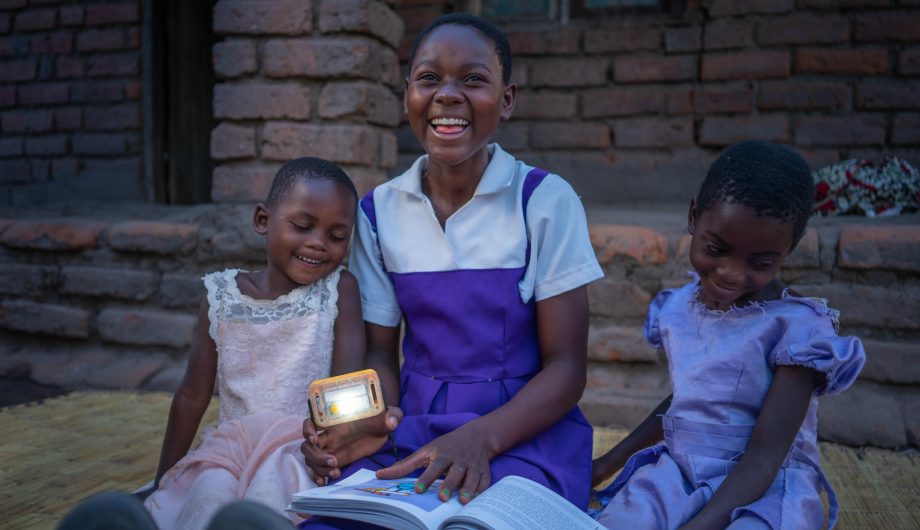 Fabriola and her sisters sit together smiling while reading a book